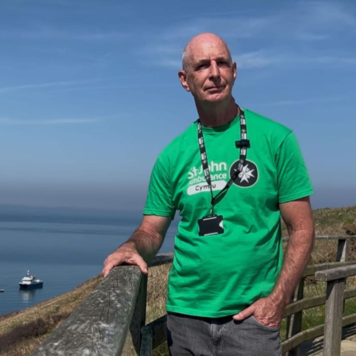 Eric wearing a bright green 'St John Ambulance Cymru' t-shirt stands outdoors on his Walk Around Wales.