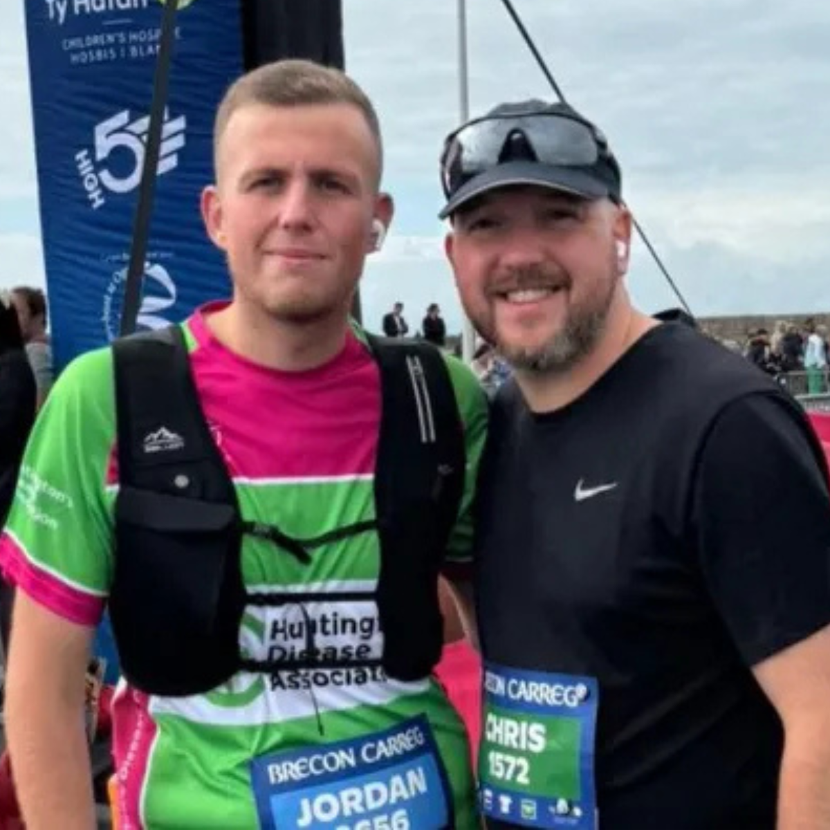 Two runners standing next to each other in running gear. Both have race bibs on with their names and race numbers.