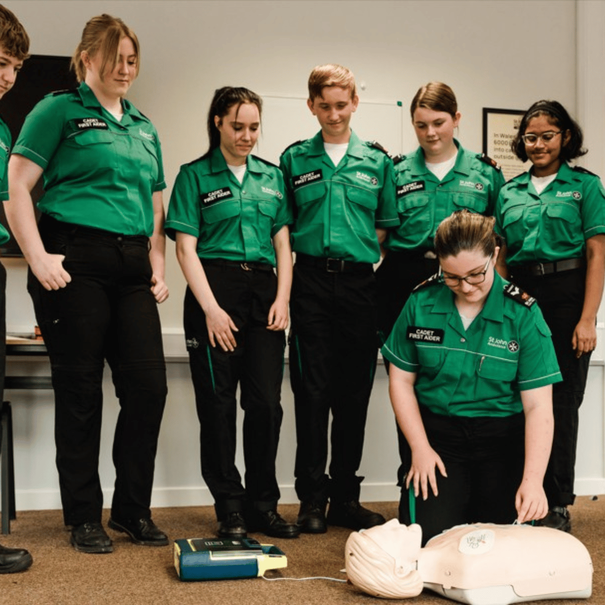 Cadet first aiders observing another cadet perform first aid and CPR and defibrillator practice on a training manikin.
