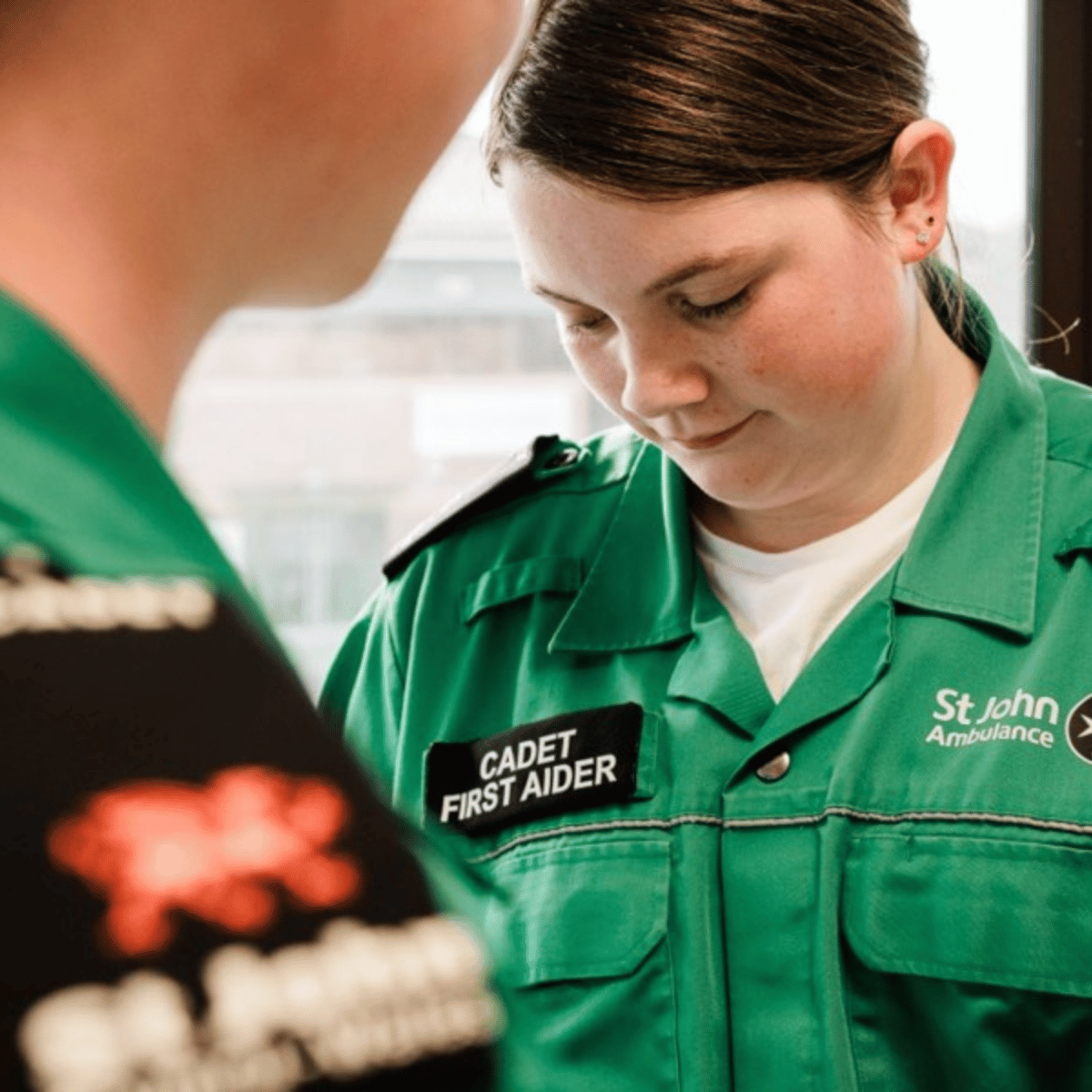 A St John Ambulance Cymru Cadet First Aider in green uniform looking down to the floor.