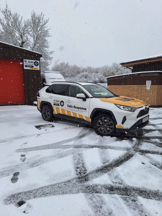A white St John Ambulance Cymru falls response vehicle parked on a snowy surface. The vehicle emblazoned with the charity's name and maltese cross logo.