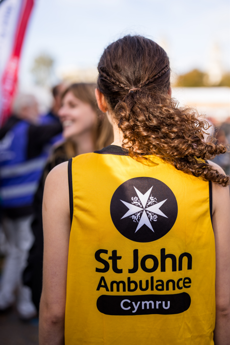 Runner for Cardiff Half Marathon wearing a St John Ambulance Cymru vest. She has long brown hair and is facing away from the camera.
