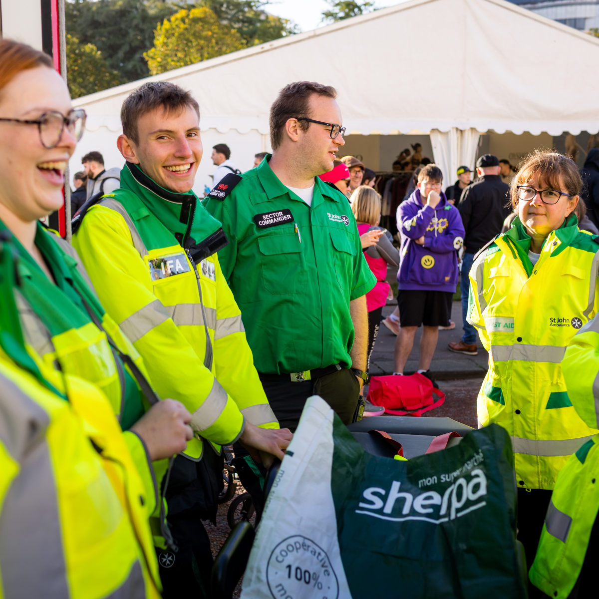 St John Ambulance Cymru volunteers smiling and laughing outside the Cardiff Half Marathon medical tent. They are all in uniform and are standing in a circle.
