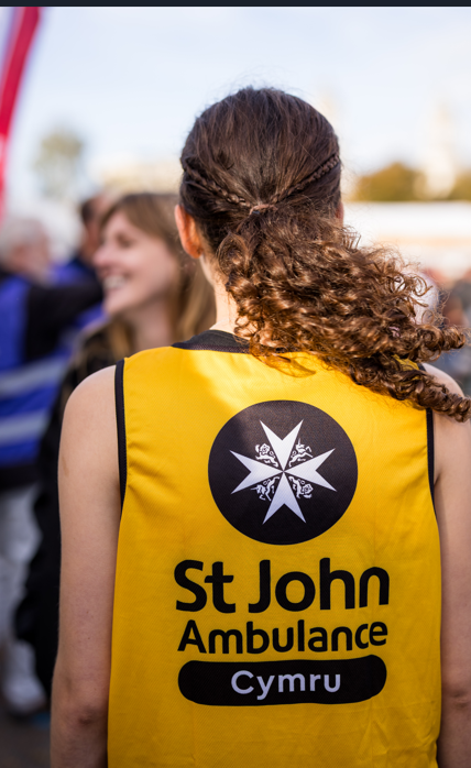 Runner for Cardiff Half Marathon wearing a St John Ambulance Cymru vest. She has long brown hair and is facing away from the camera.