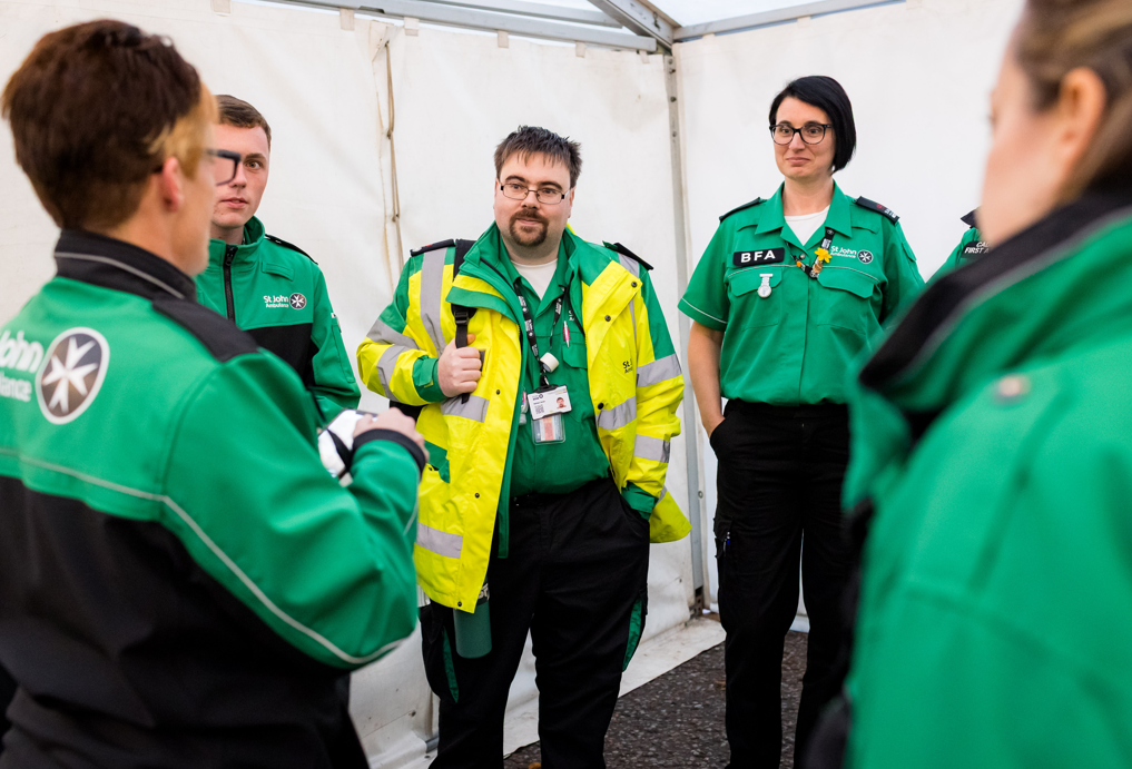 St John Ambulance Cymru staff in their green uniform, in the medical tent at the Cardiff Half Marathon. They are listening to one of the first aiders and having a brief for the day ahead.